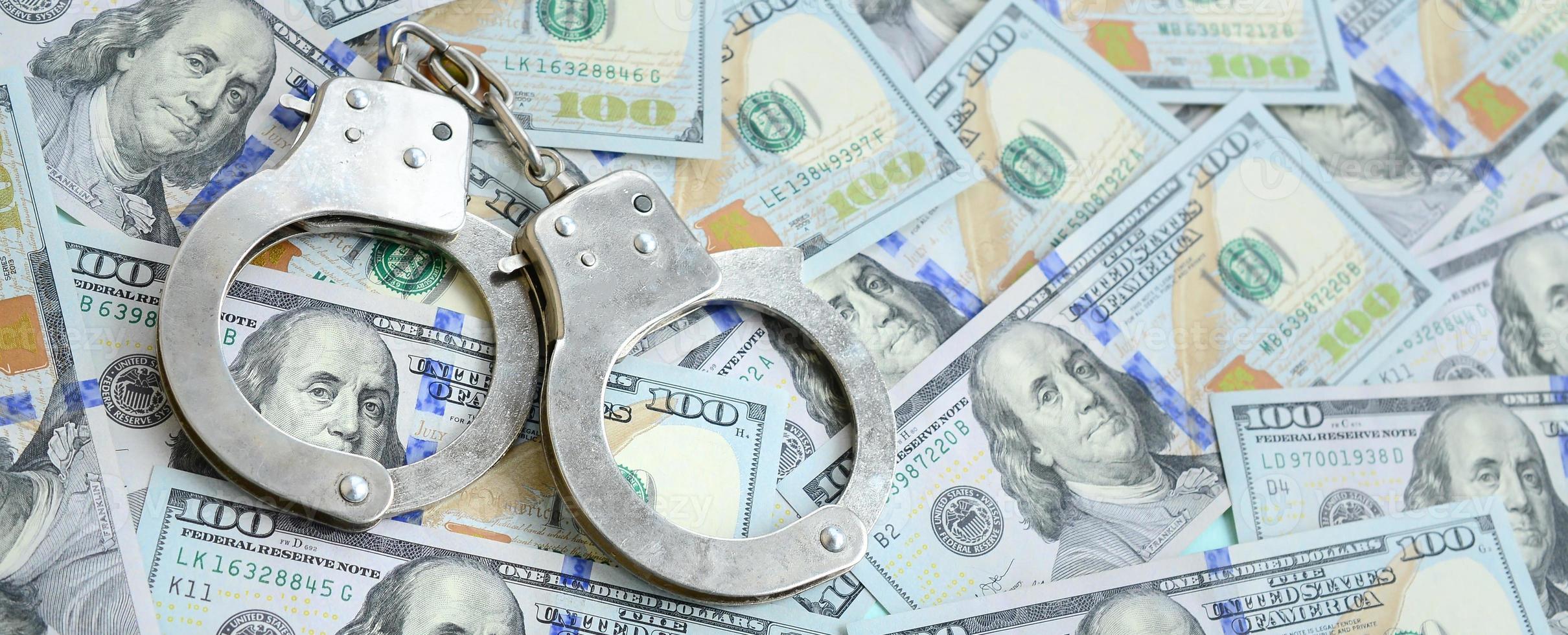 Silver police handcuffs lies on a many dollar bills photo