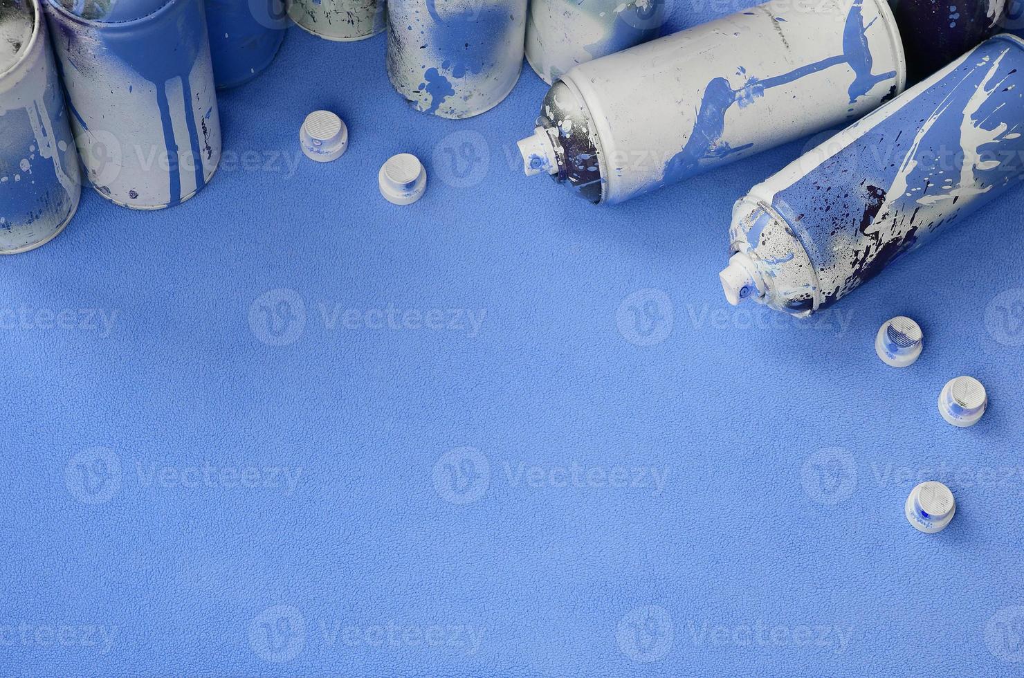 Some used blue aerosol spray cans and nozzles with paint drips lies on a blanket of soft and furry light blue fleece fabric. Classic female design color. Graffiti hooliganism concept photo