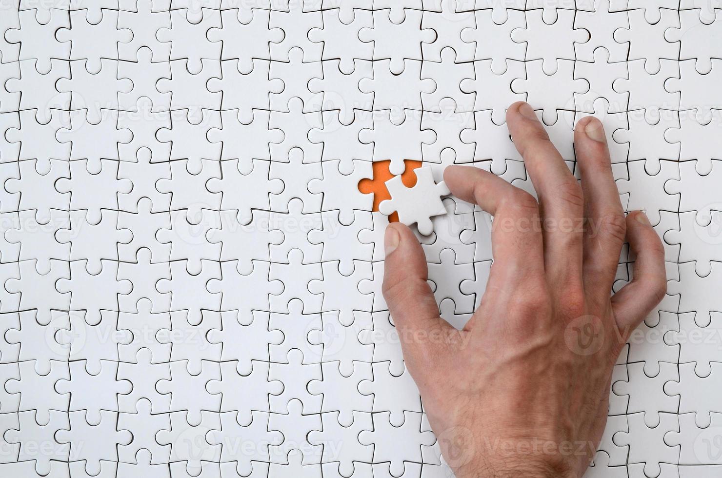 The texture of a white jigsaw puzzle in the assembled state with one missing element that the male hand puts in photo