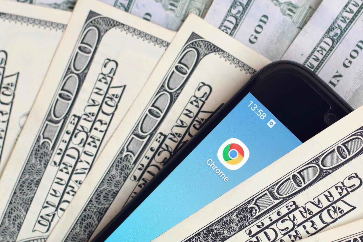 KHARKOV, UKRAINE - JULY 2, 2021 Smartphone screen with Google chrome app and lot of hundred dollar bills. Business and social networking concept photo