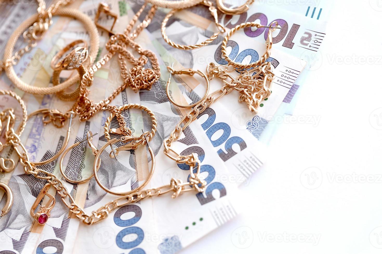 Many expensive golden jewerly rings, earrings and necklaces with big amount of Ukrainian money bills. Pawnshop or jewerly shop concept. Jewelry trading photo