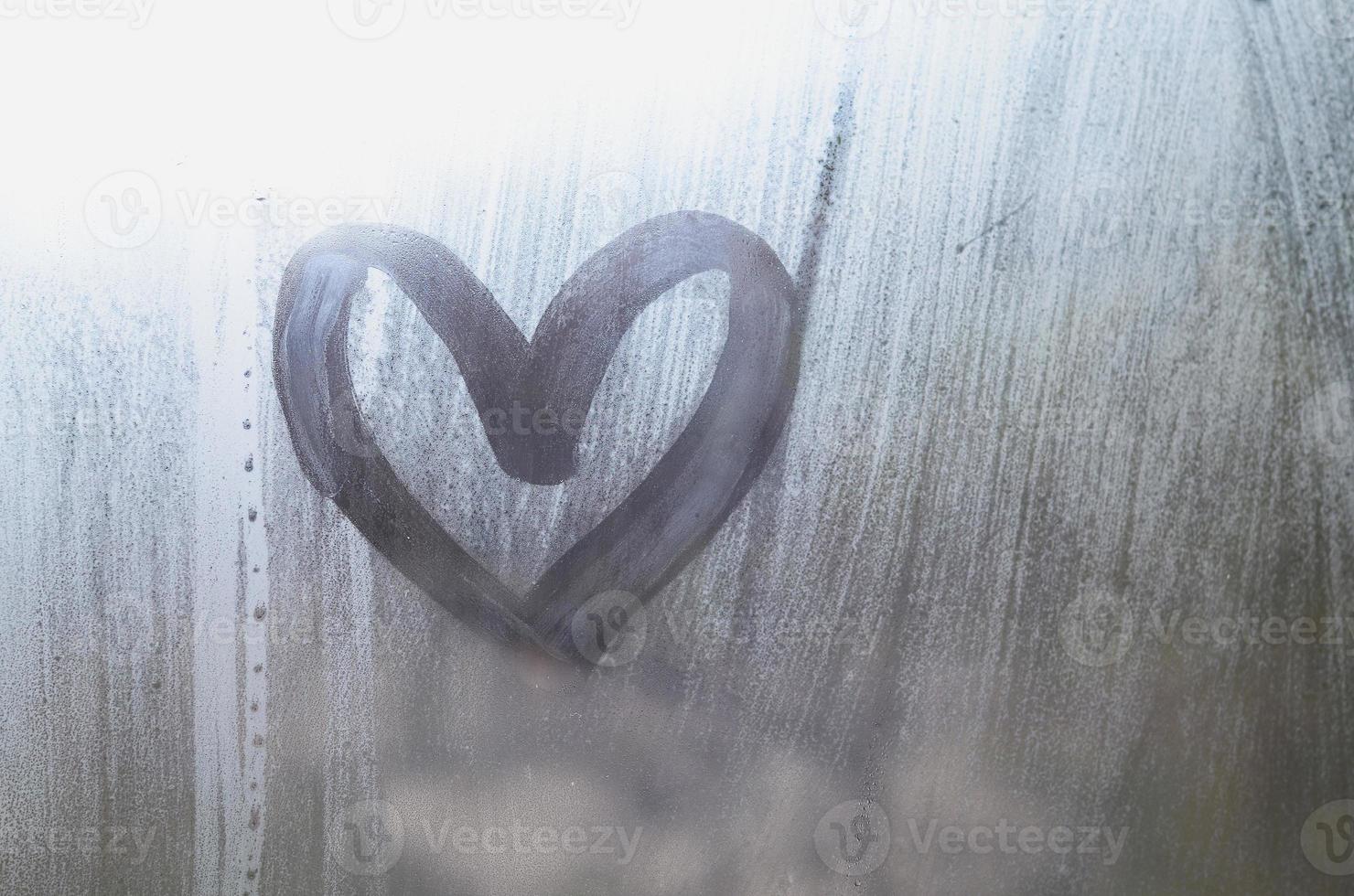 A heart-shaped drawing drawn by a finger on a misted glass in rainy weather photo