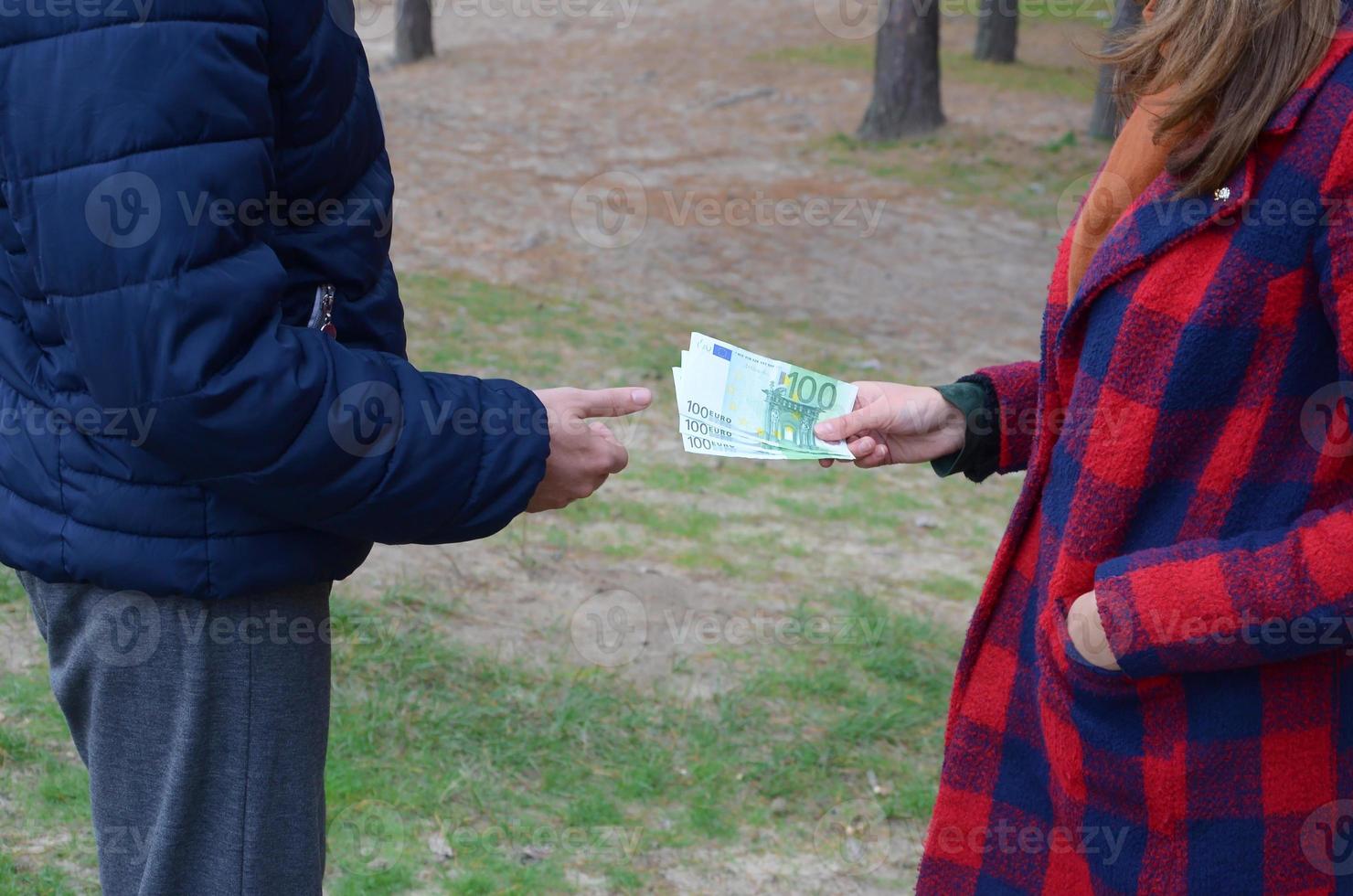 Girl transfers euro bills to the hands of a young guy in forest. Concept of robbery or illegal deal transaction photo