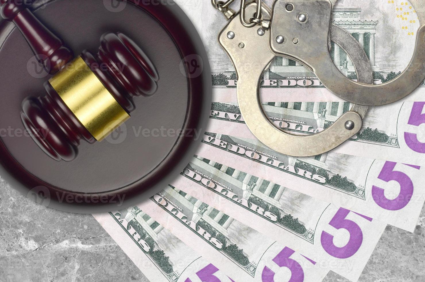 5 US dollars bills and judge hammer with police handcuffs on court desk. Concept of judicial trial or bribery. Tax avoidance photo