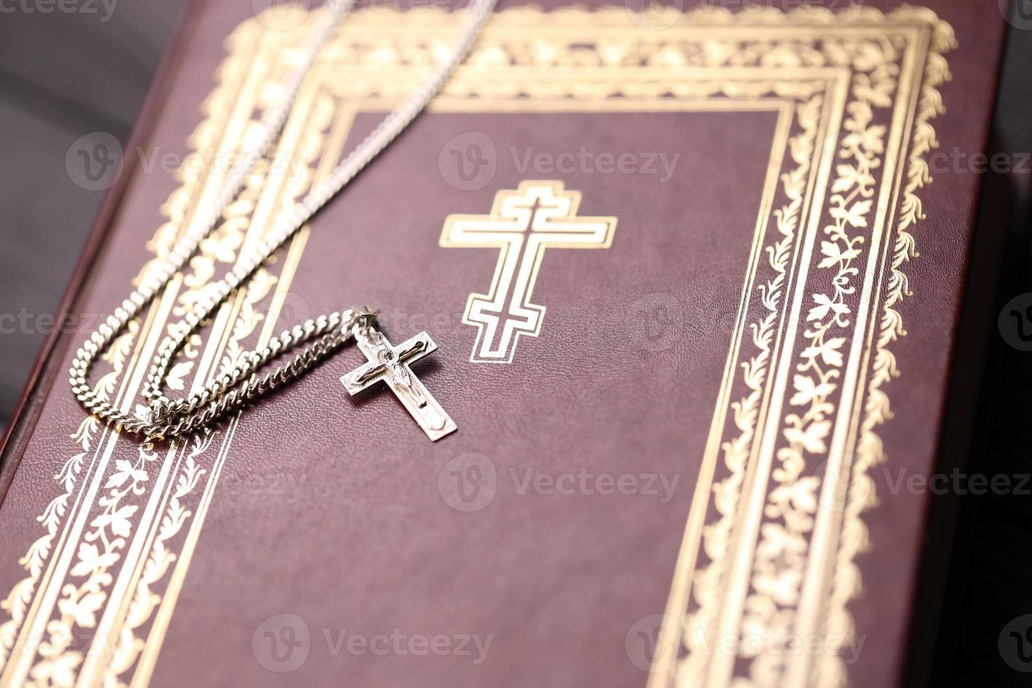 Silver necklace with crucifix cross on christian holy bible book on black wooden table. Asking blessings from God with the power of holiness, which brings luck photo