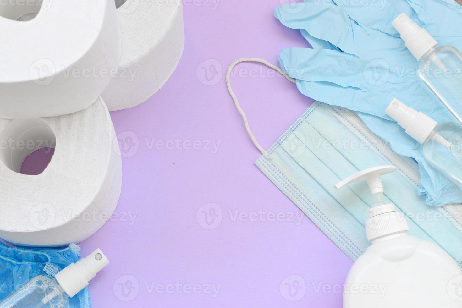 conjunto de artículos importantes para la cuarentena de covid-19. papel higiénico, guantes desechables de goma con mascarilla quirúrgica y desinfectante de manos con botella de jabón líquido sobre fondo lila foto