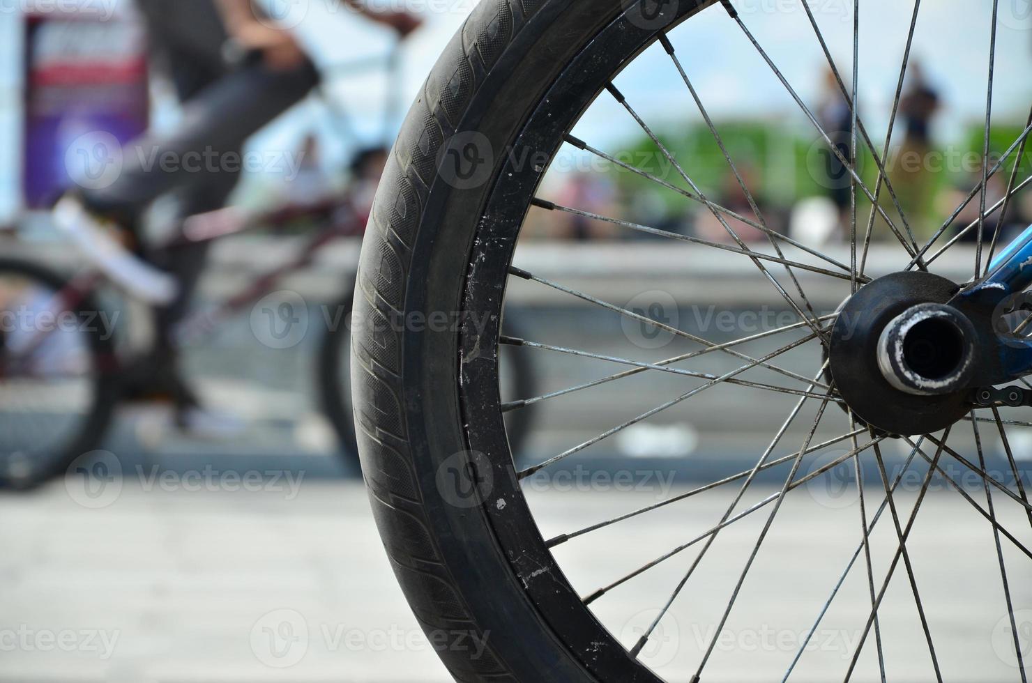 A BMX bike wheel against the backdrop of a blurred street with cycling riders. Extreme Sports Concept photo