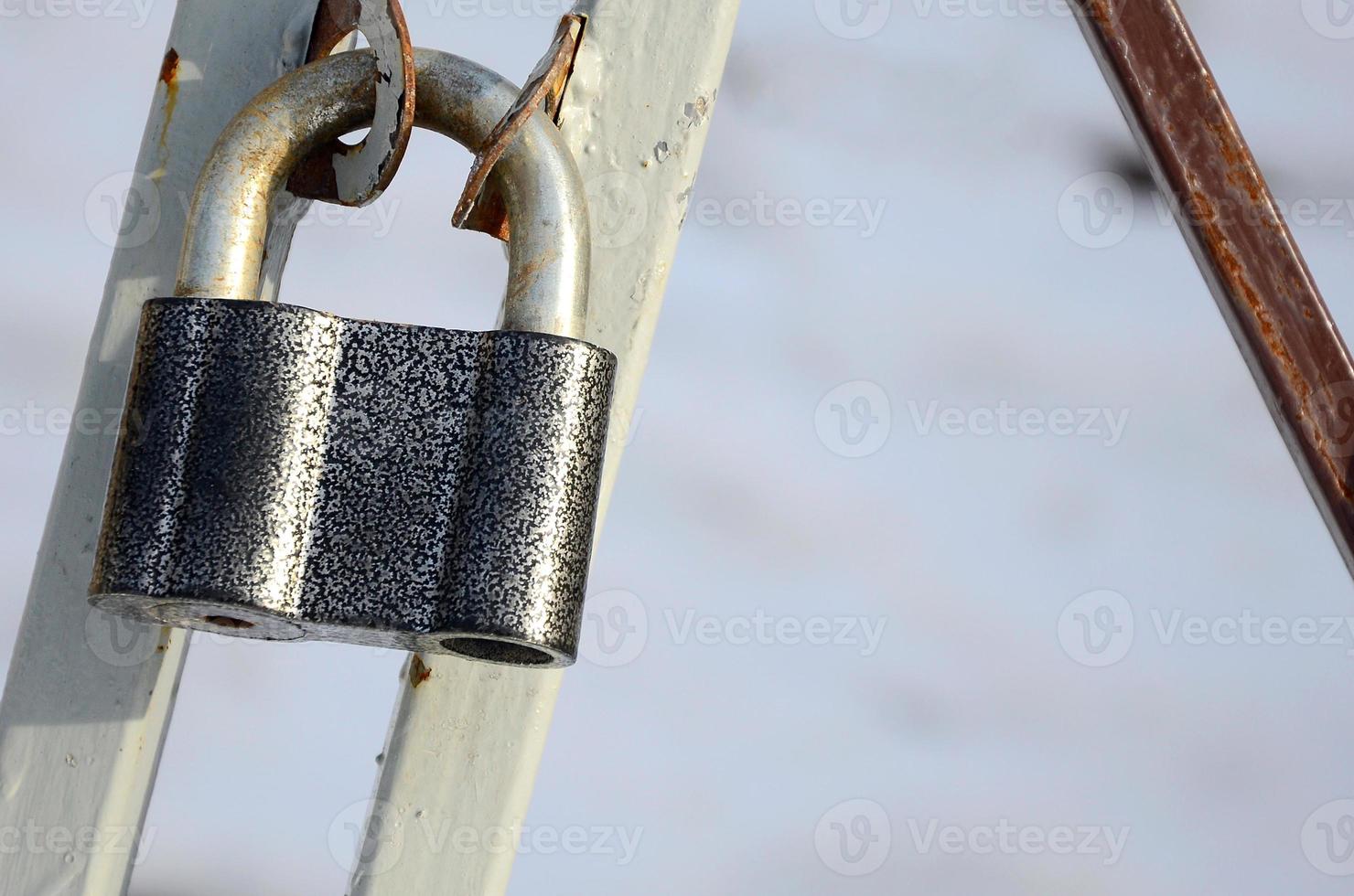 A large gray padlock hangs on a metal gate photo