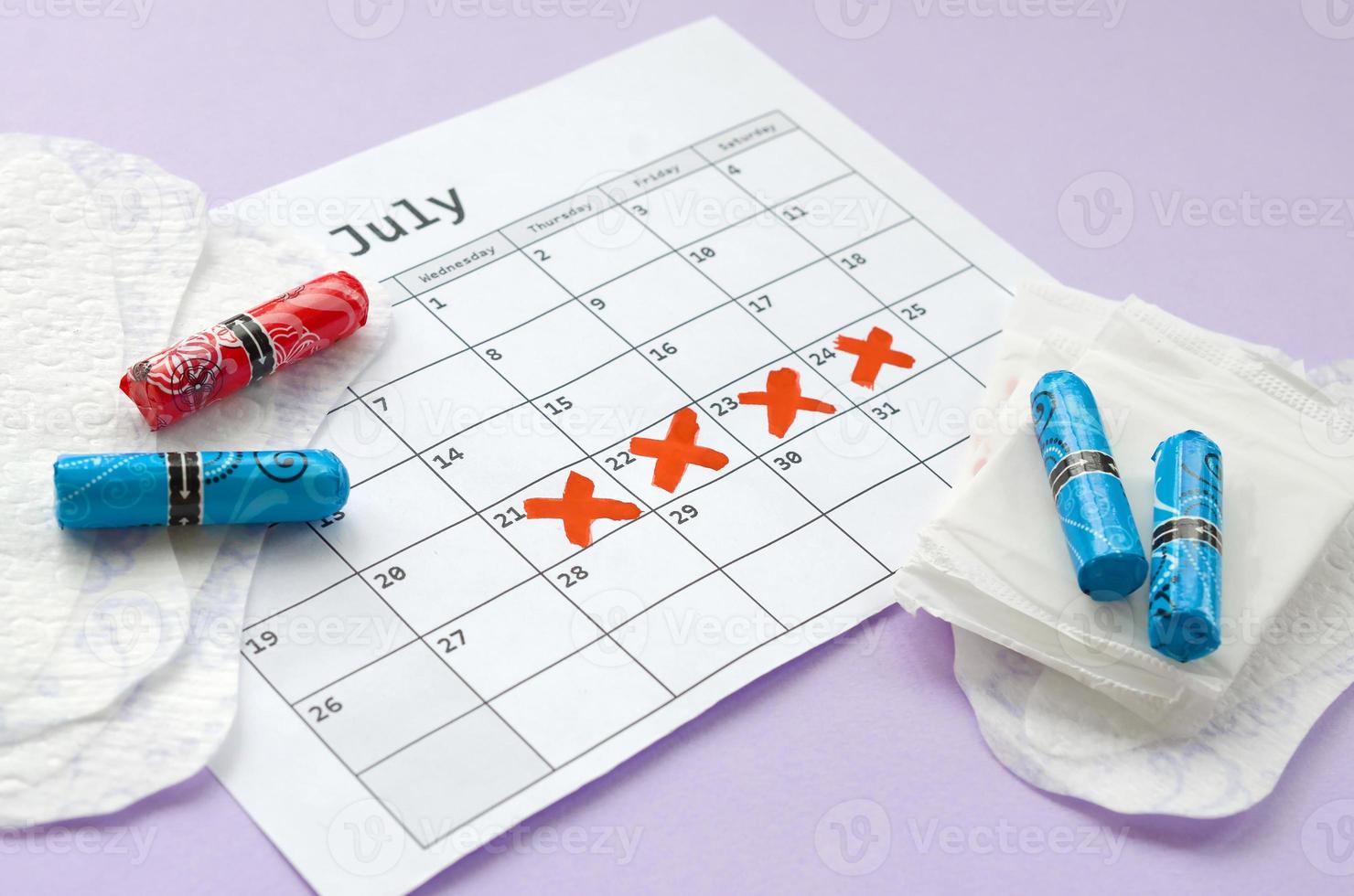 almohadillas menstruales y tampones en el calendario del período de menstruación con marcas de cruz roja sobre fondo lila foto