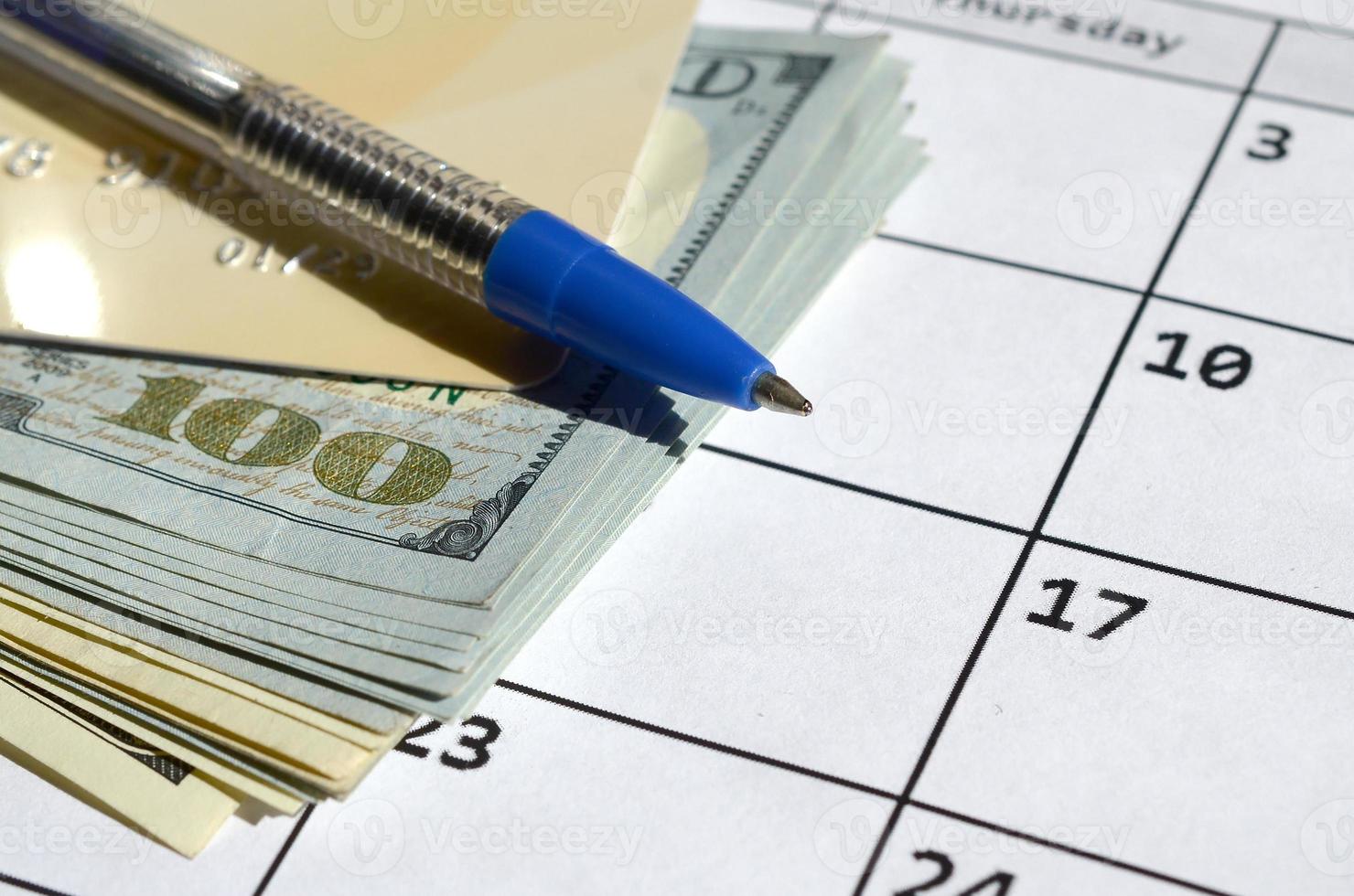 Pen and credit card on many hundred US dollar bills on calendar page close up photo