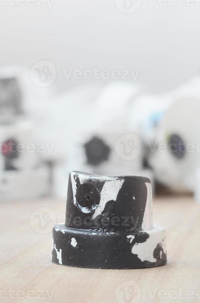 Several plastic nozzles from a paint sprayer that lie on a wooden surface against a gray wall background. The caps are smeared in black paint. The concept of street art and graffiti photo