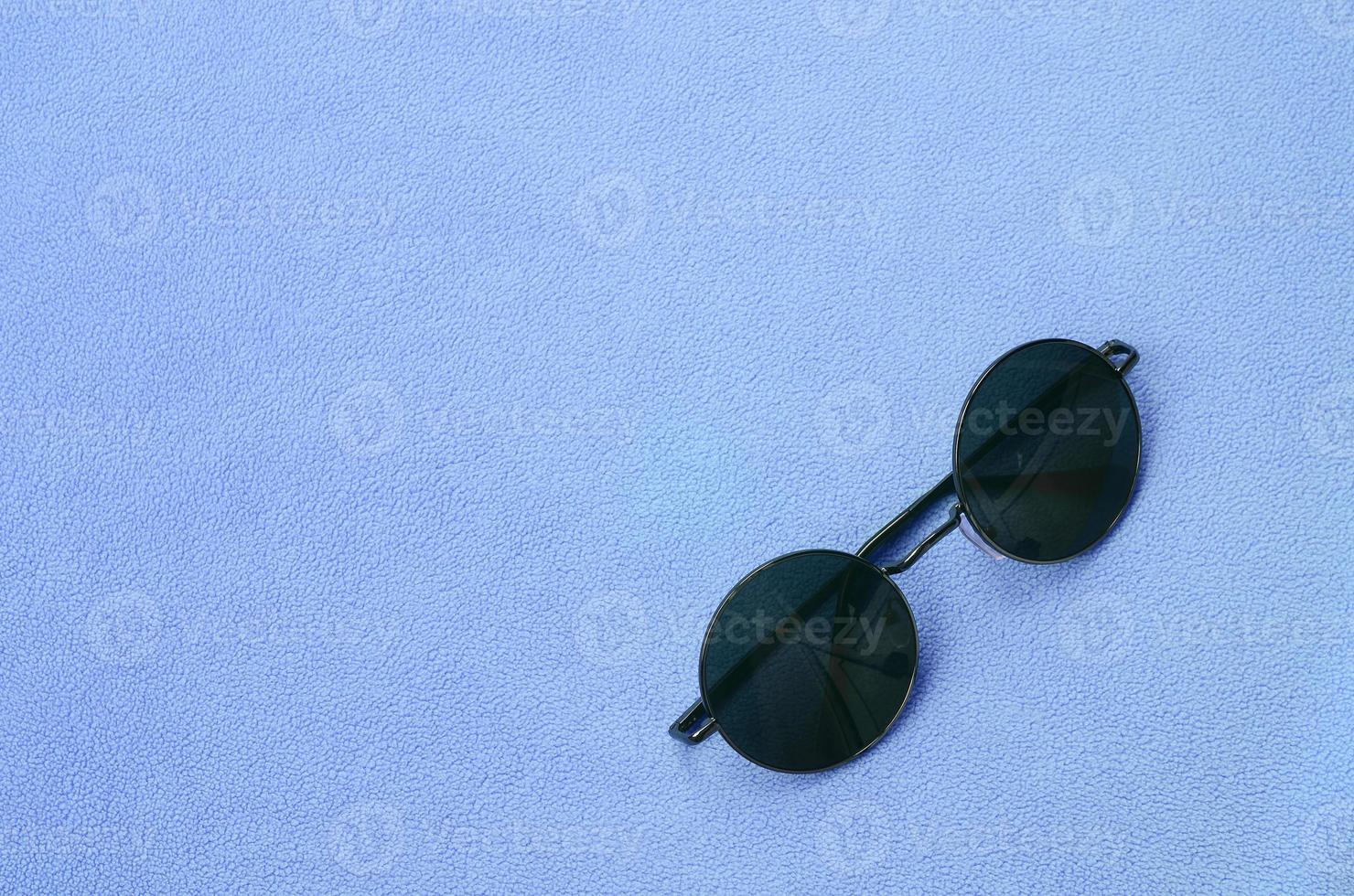 elegantes gafas de sol negras con gafas redondas se encuentran sobre una manta hecha de suave y esponjosa tela de lana azul claro. imagen de fondo de moda en colores femeninos foto