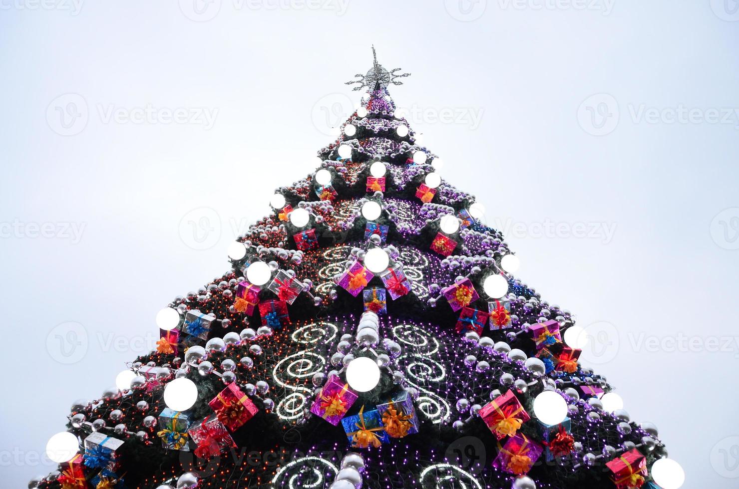 A fragment of a huge Christmas tree with many ornaments, gift boxes and luminous lamps. Photo of a decorated Christmas tree close-up with copy space