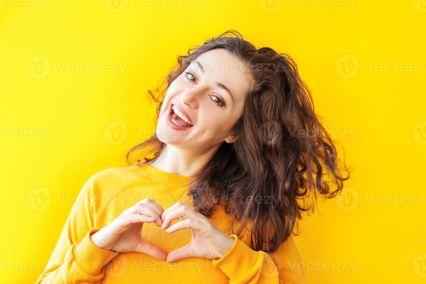 Love, heart shape, peace. Beauty portrait young happy positive woman showing heart sign with hands on yellow background isolated. European girl. Positive human emotion facial expression body language. photo