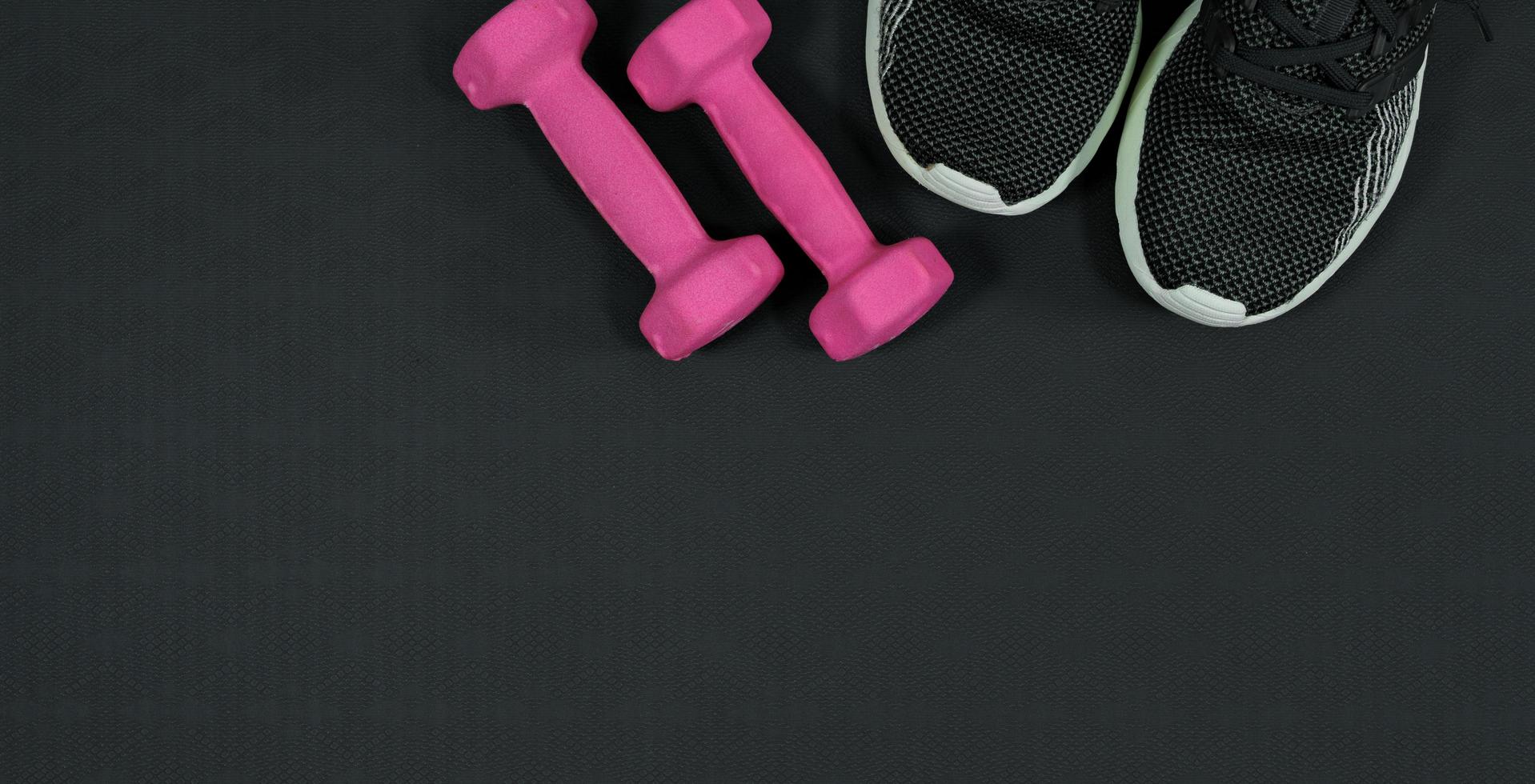 pink dumbbell and sports shoe background on black rubber background.fitness equipment background concept photo