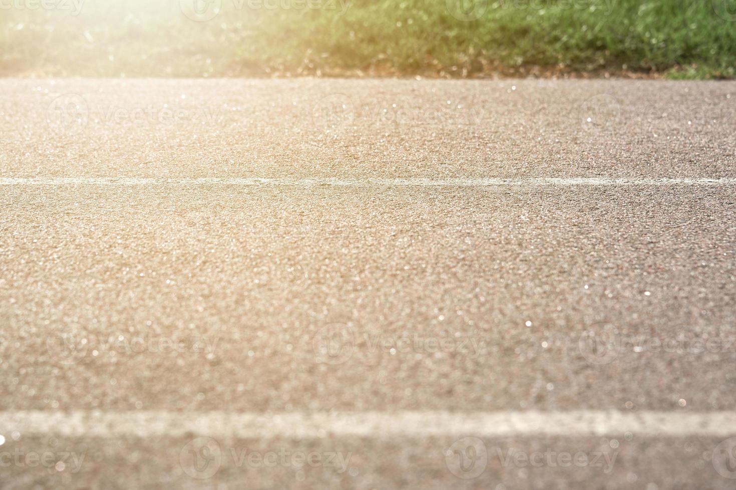 Texture paved road with markings illuminated by bright sunlight on the background of green grass. Part of the photo is in blur.