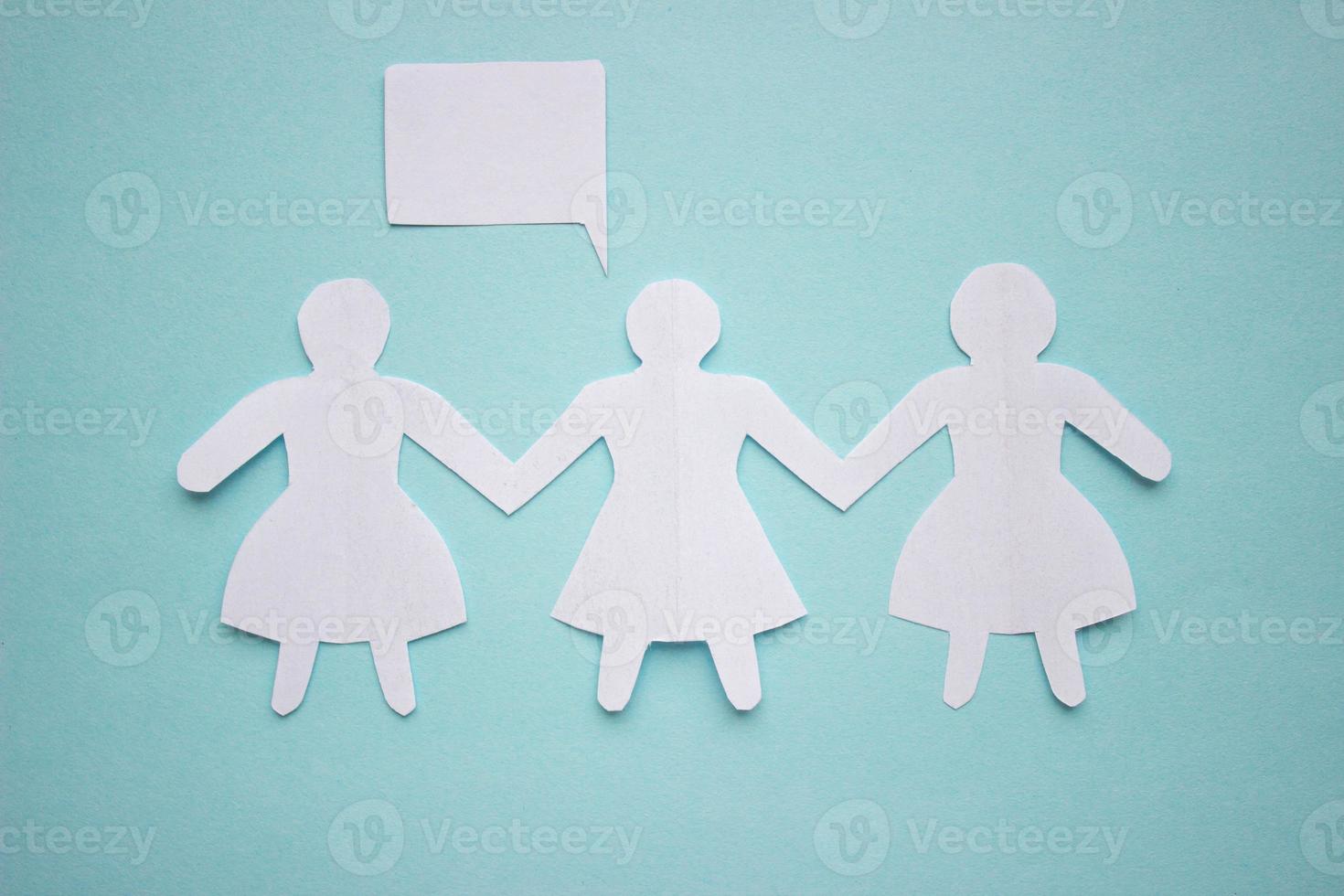 Silhouette of three girls in dresses holding hands, cut out of white paper. With speech-bubble. In the center of the photo on a blue background