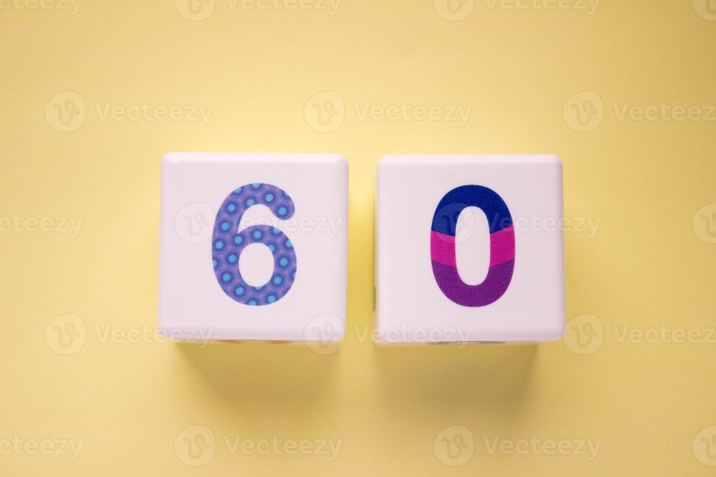 Close-up photo of a white plastic cubes with a colorful number 60 on a yellow background. Object in the center of the photo