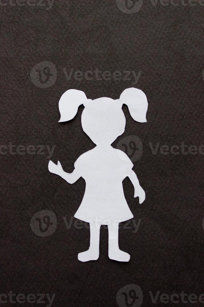 The form of a girl in a dress and with ponytails made of white paper, cut by hand. In the center of vertical photo