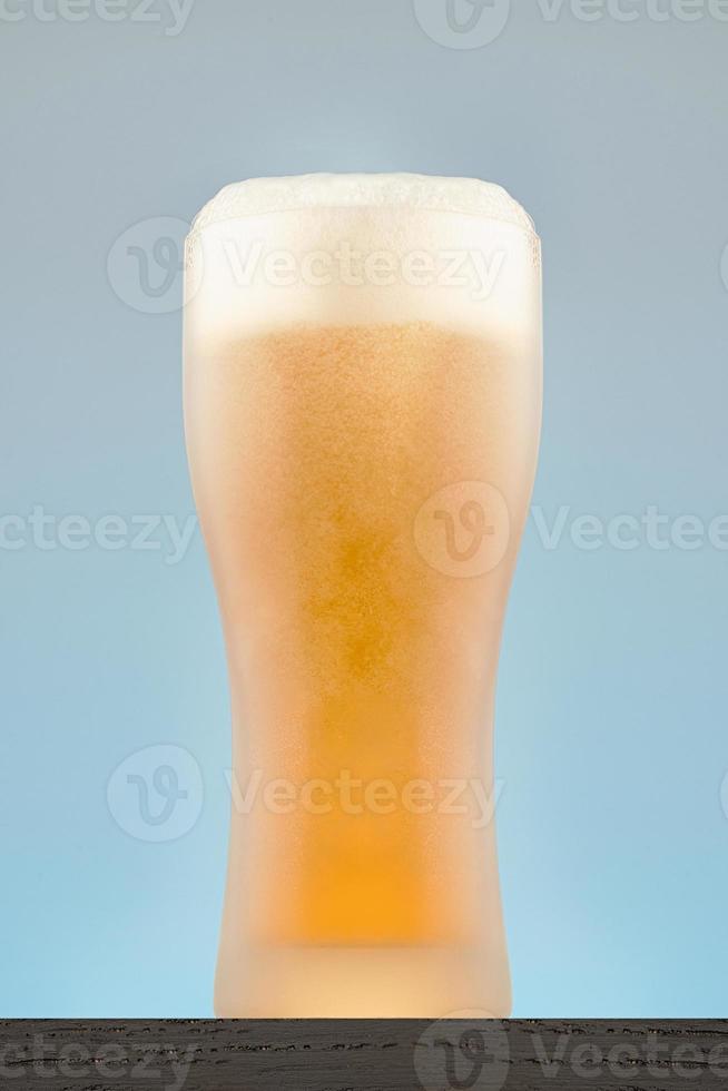vaso de cerveza empañado con espuma. primer plano de vaso de cerveza sobre un fondo gris-azul. foto