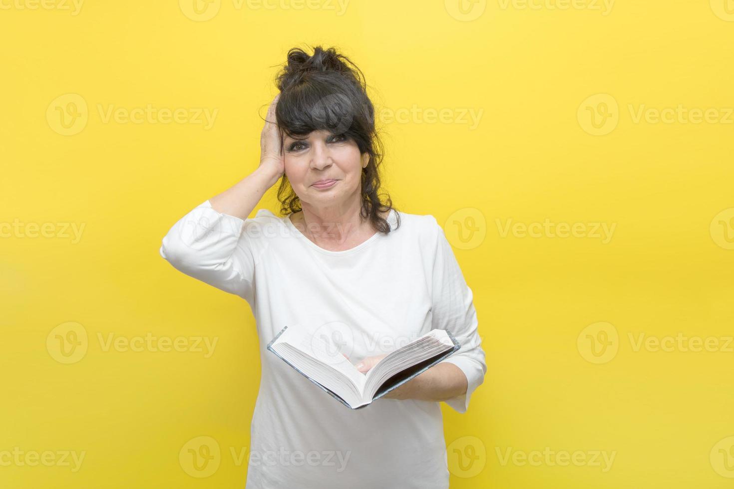 sympathetic elderly woman holds a book in her hand, clutches her head in emotions from what is written in the book photo