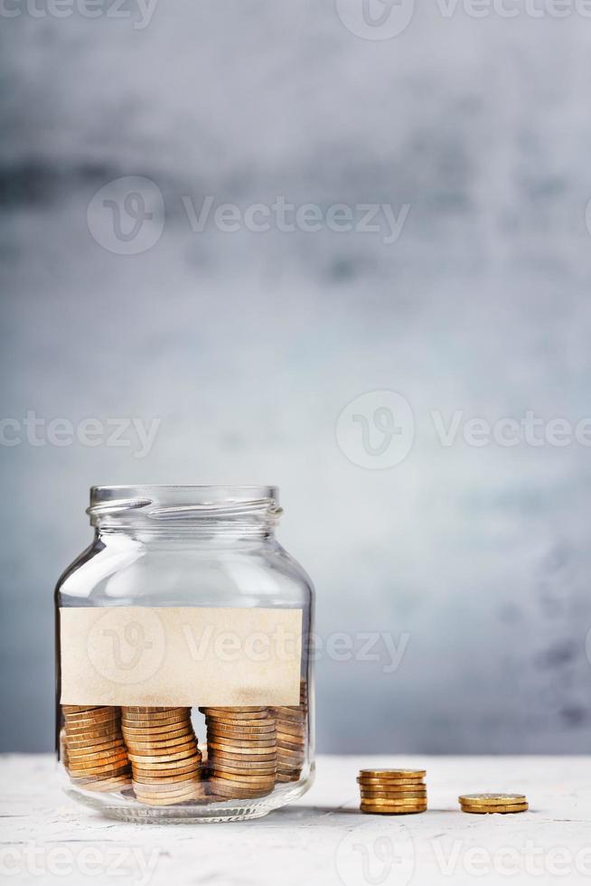 Glass Jar with gold coins and text sticker on a grey background with free space for text. photo