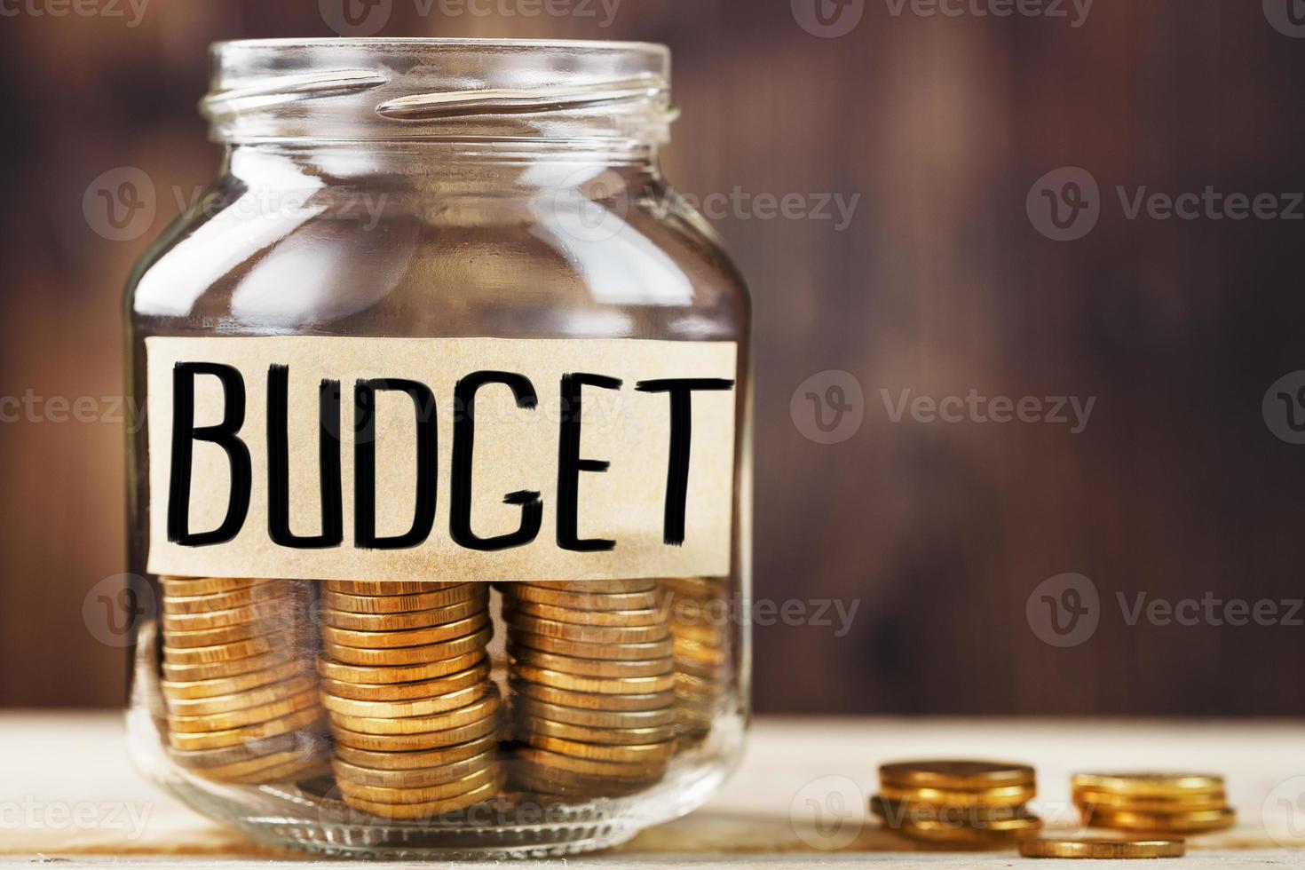 Glass jar with money and a sticker with the words BUDGET, on a wooden table. photo