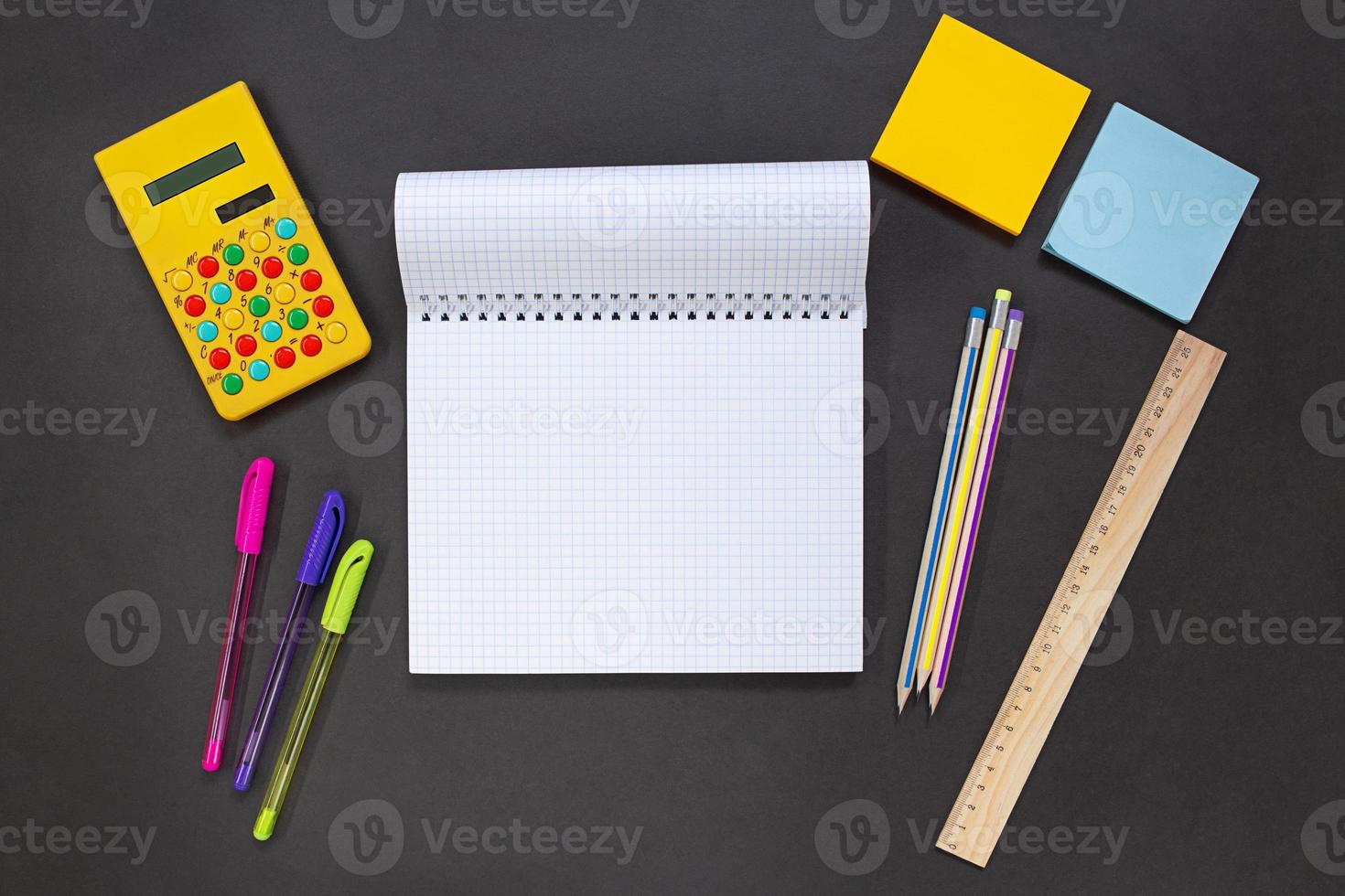 Notepad, yellow calculator, pens and pencils, stickers, ruler on a black background. Stationery for business, study. Concept back to school, finance. Copy space photo