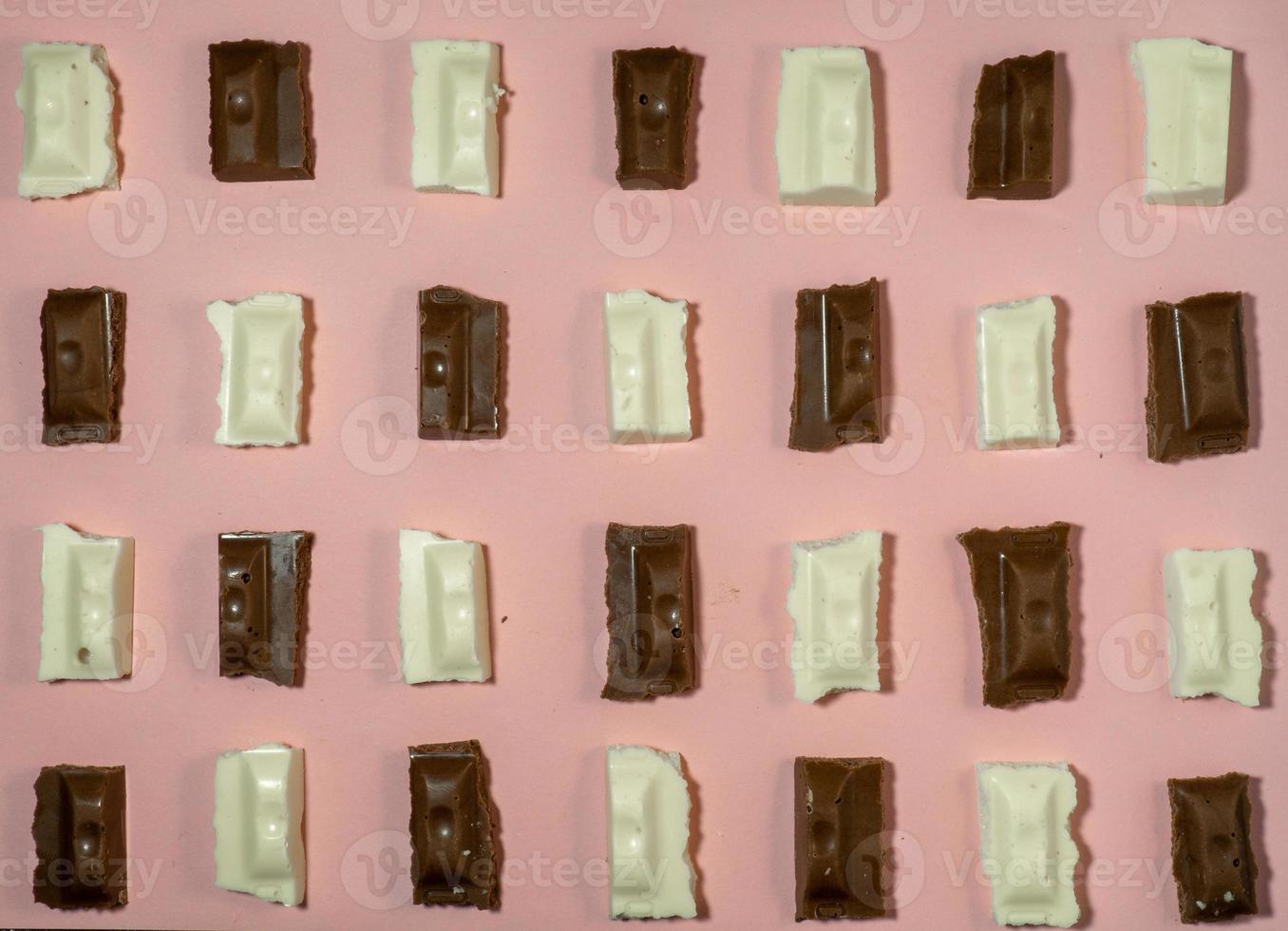 Slices of black and white chocolate on a pink background. Various chocolates on the table. photo