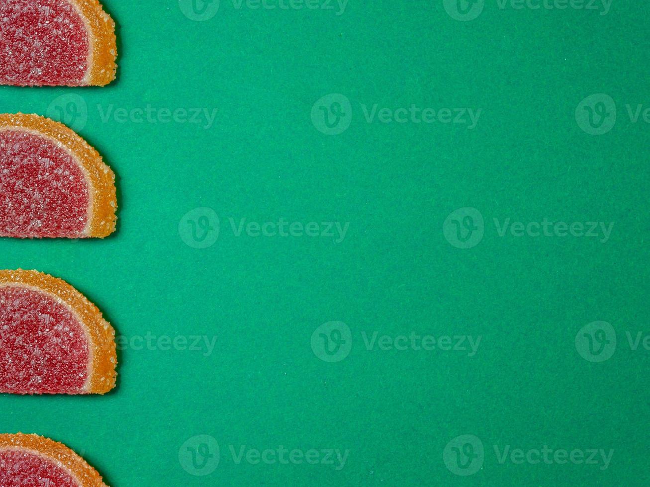 Fruit jelly in the form of orange slices on a green surface. Background from sweets. photo