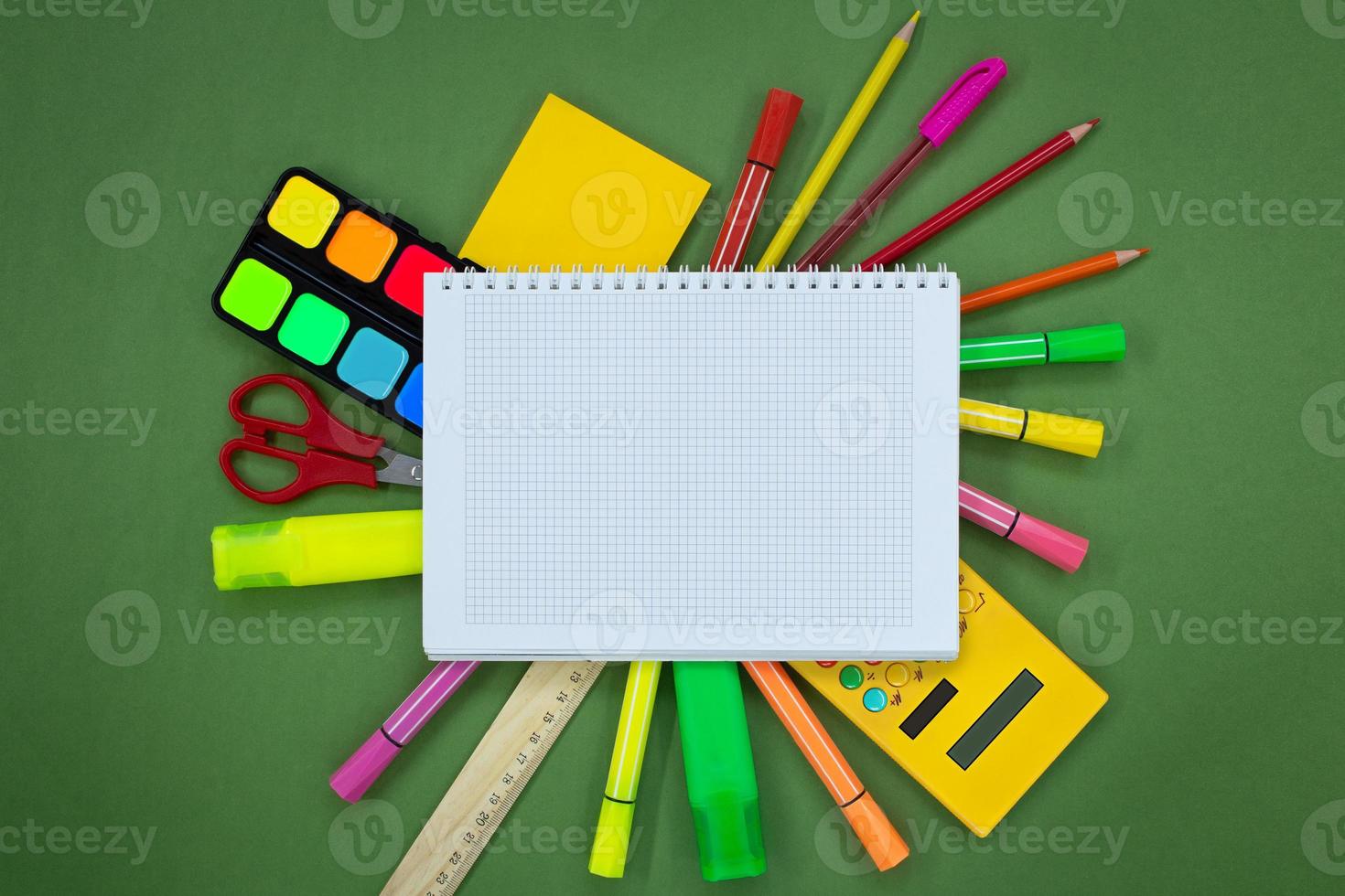 Set of stationery around a notebook on a green background. Pens, markers, felt-tip pens, scissors, calculator, paints. Back to school concept. Copy space photo