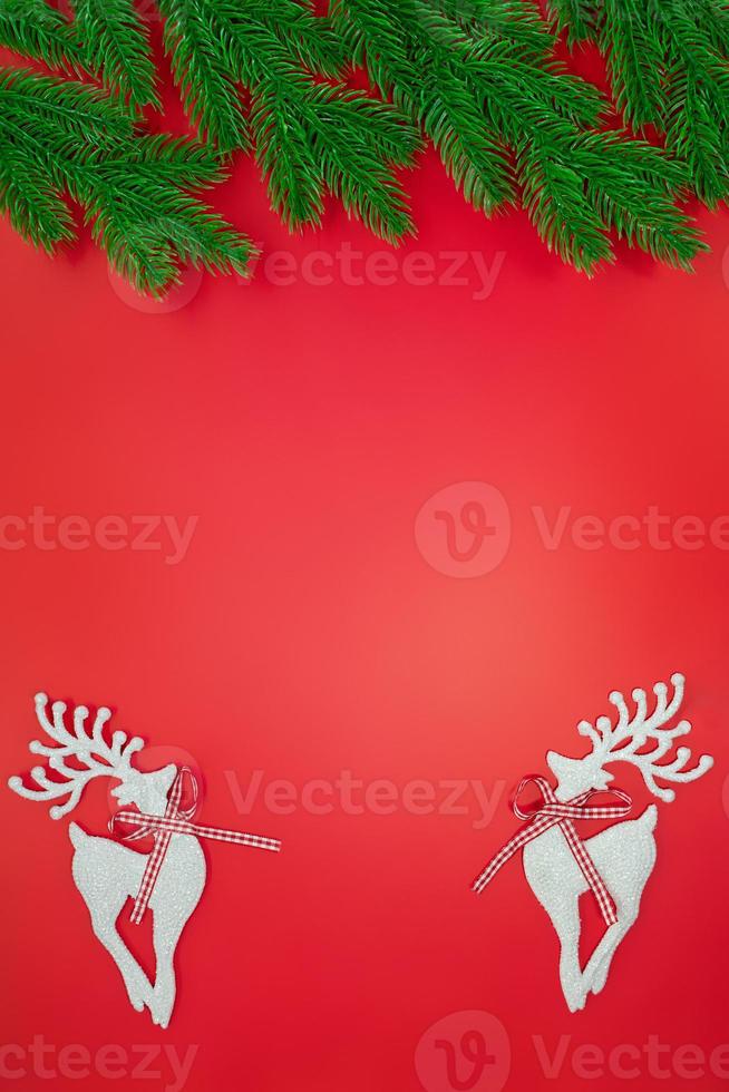 White shiny deer on red background with green branches of Christmas tree. New Year. Copy space photo