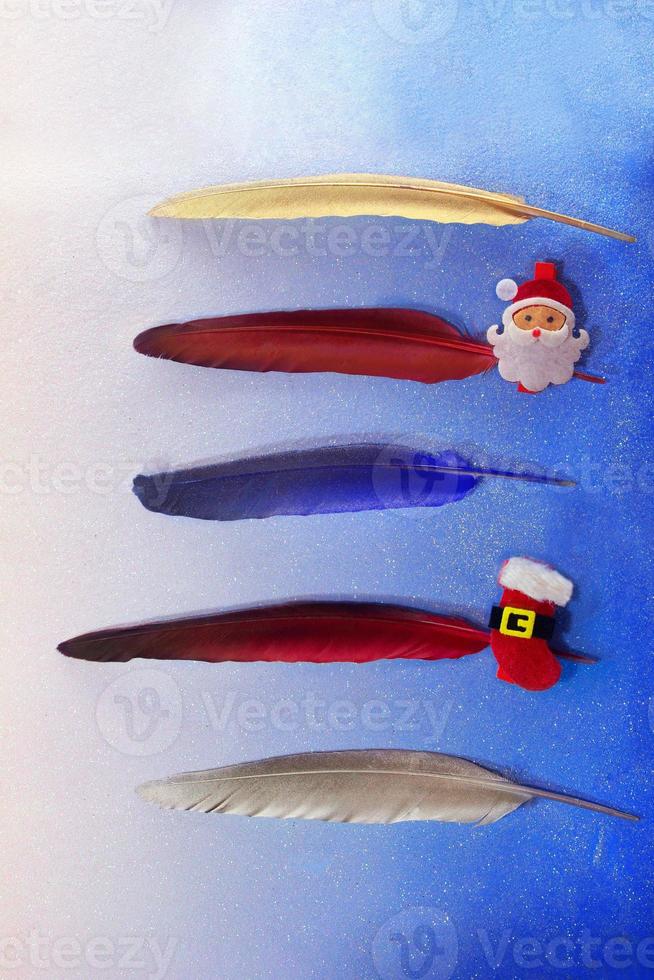 Gold, red, blue, silver feathers with pin with santa claus and a boot on a blue background. For list, write text, planning. Five lines. Christmas and New year photo