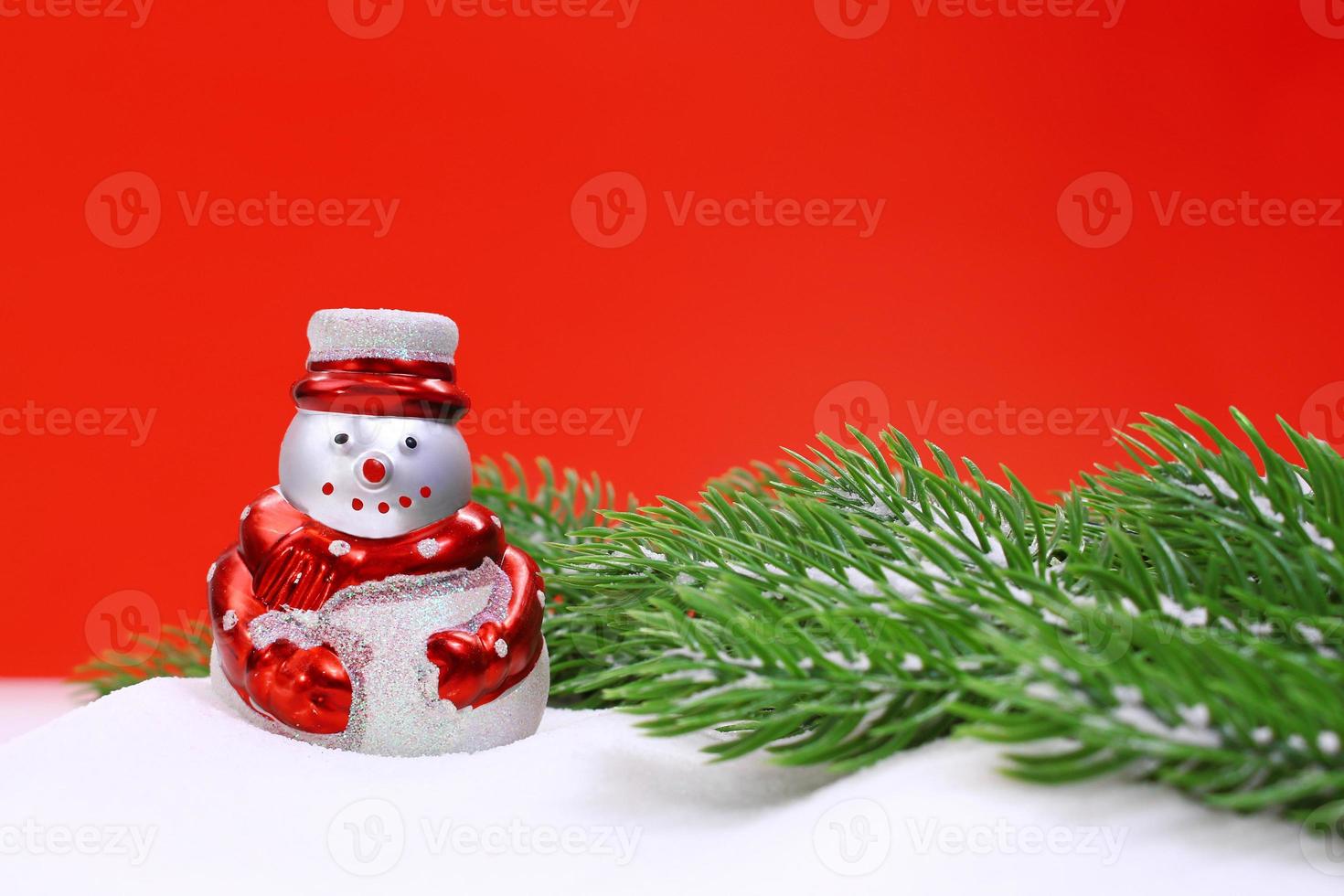 Snowman in the snow and green spruce branches on red background. Christmas, New Year. Copy space photo