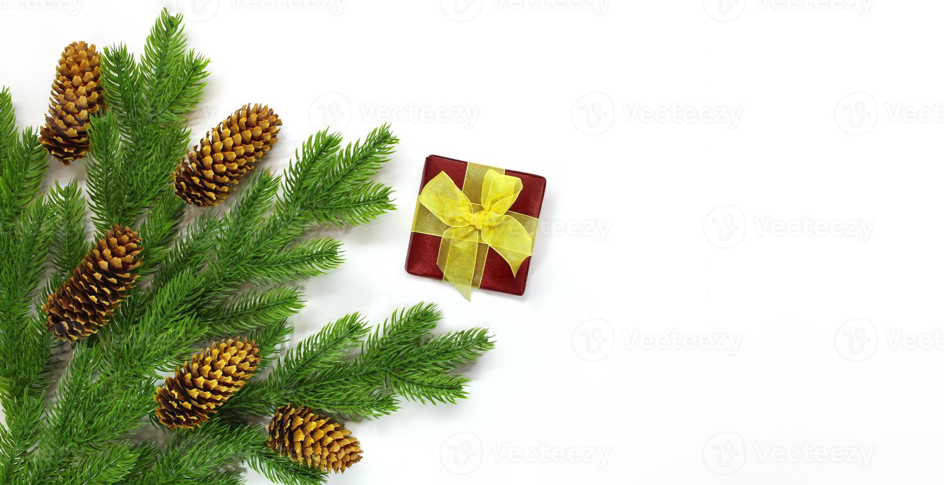 Fir branches with cones in corner and red gift box with yellow bow on white background. Christmas, New Year. Copy space photo