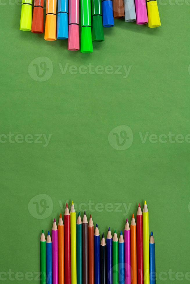 Colored felt tip pens and pencils in a row at the bottom and top or side with empty space for text on green. Back to school concept, drawing. Copy space photo
