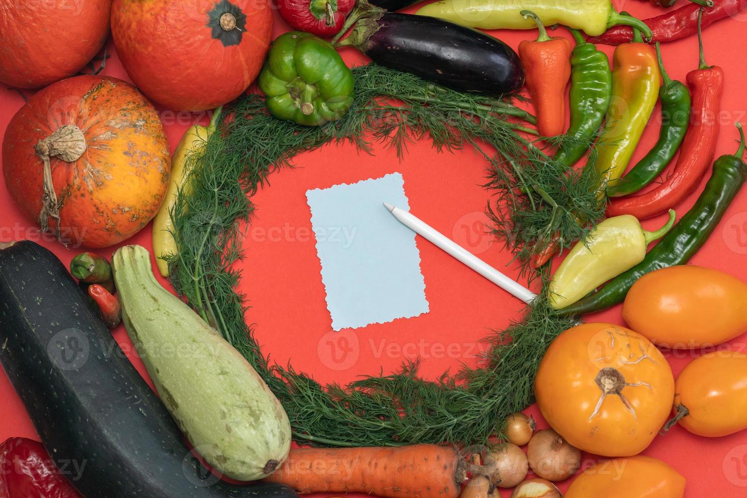Vegetables are laid out around a sheet of paper and a pencil. Empty space for text. Vegetables, empty blank for recipe on a red background. photo