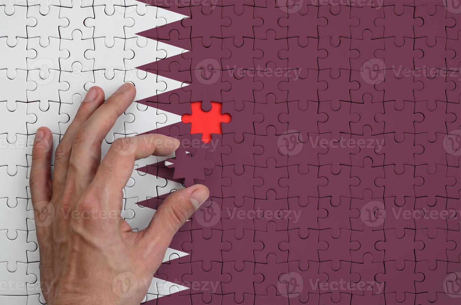 Qatar flag  is depicted on a puzzle, which the man's hand completes to fold photo