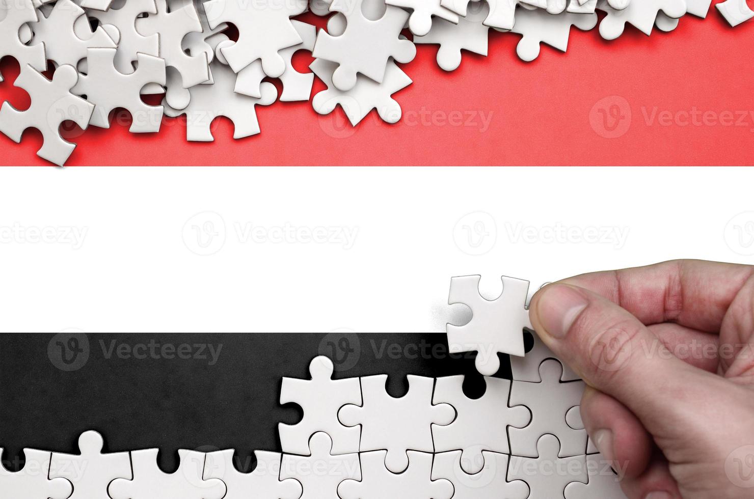 Yemen flag  is depicted on a table on which the human hand folds a puzzle of white color photo