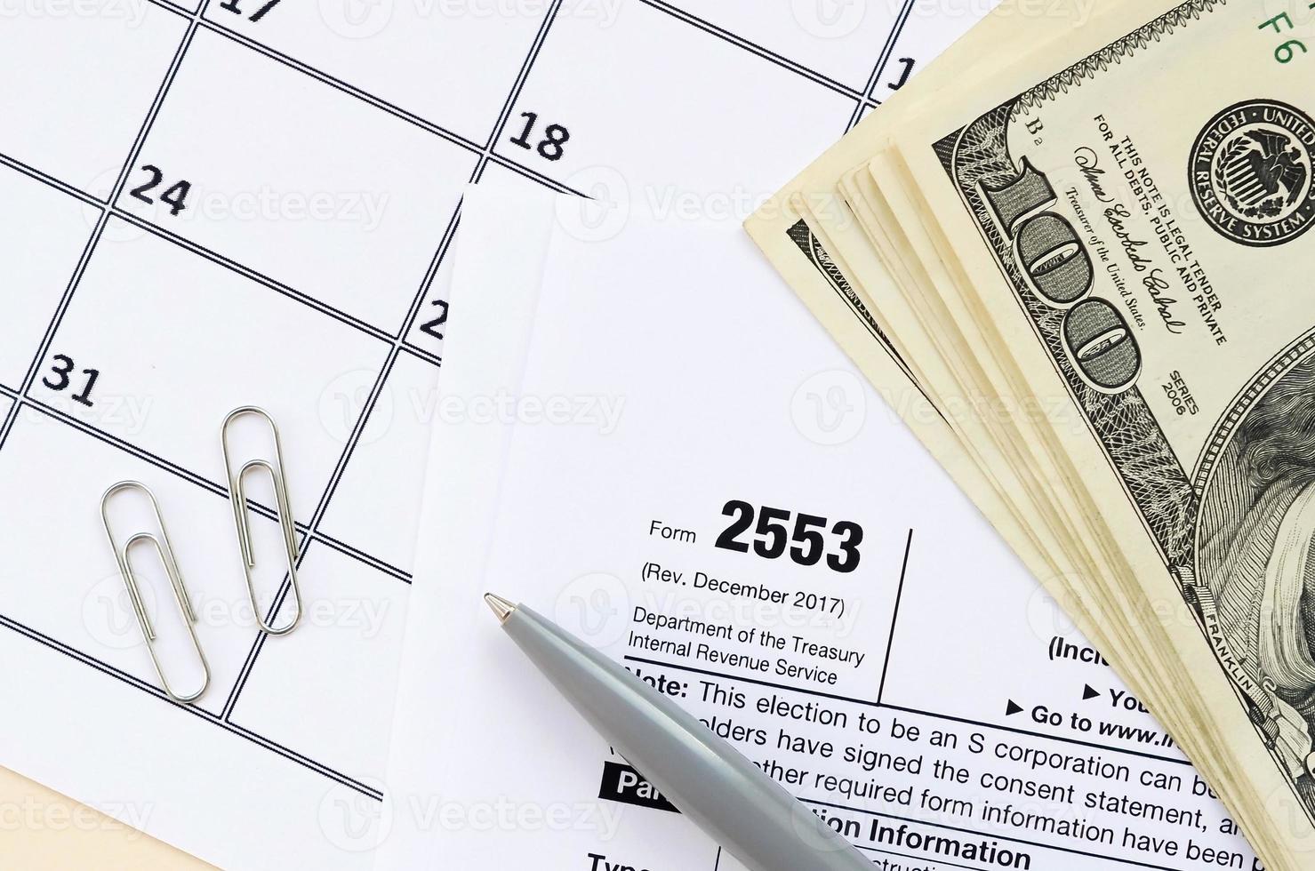 IRS Form 2553 Election by a Small Business Corporation tax blank lies with pen and many hundred dollar bills on calendar page photo