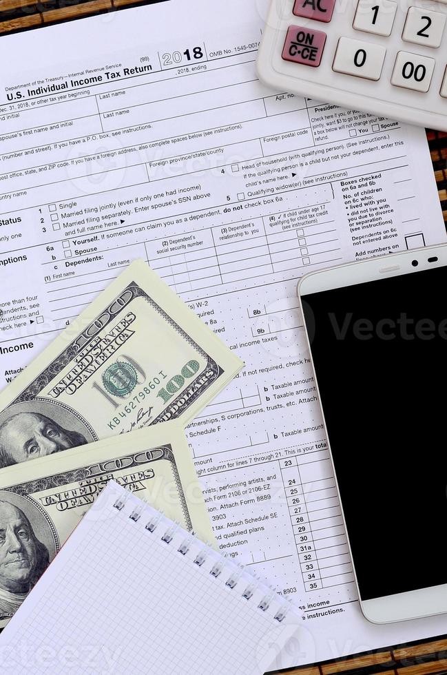 composición de elementos que se encuentran en el formulario de impuestos 1040. billetes de dólar, calculadora, teléfono inteligente, clip y bloc de notas. la hora de pagar impuestos foto