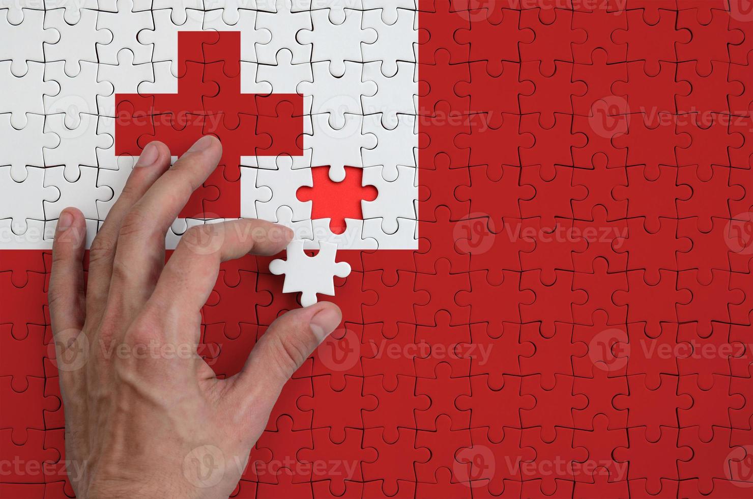 la bandera de tonga se representa en un rompecabezas, que la mano del hombre completa para doblar foto