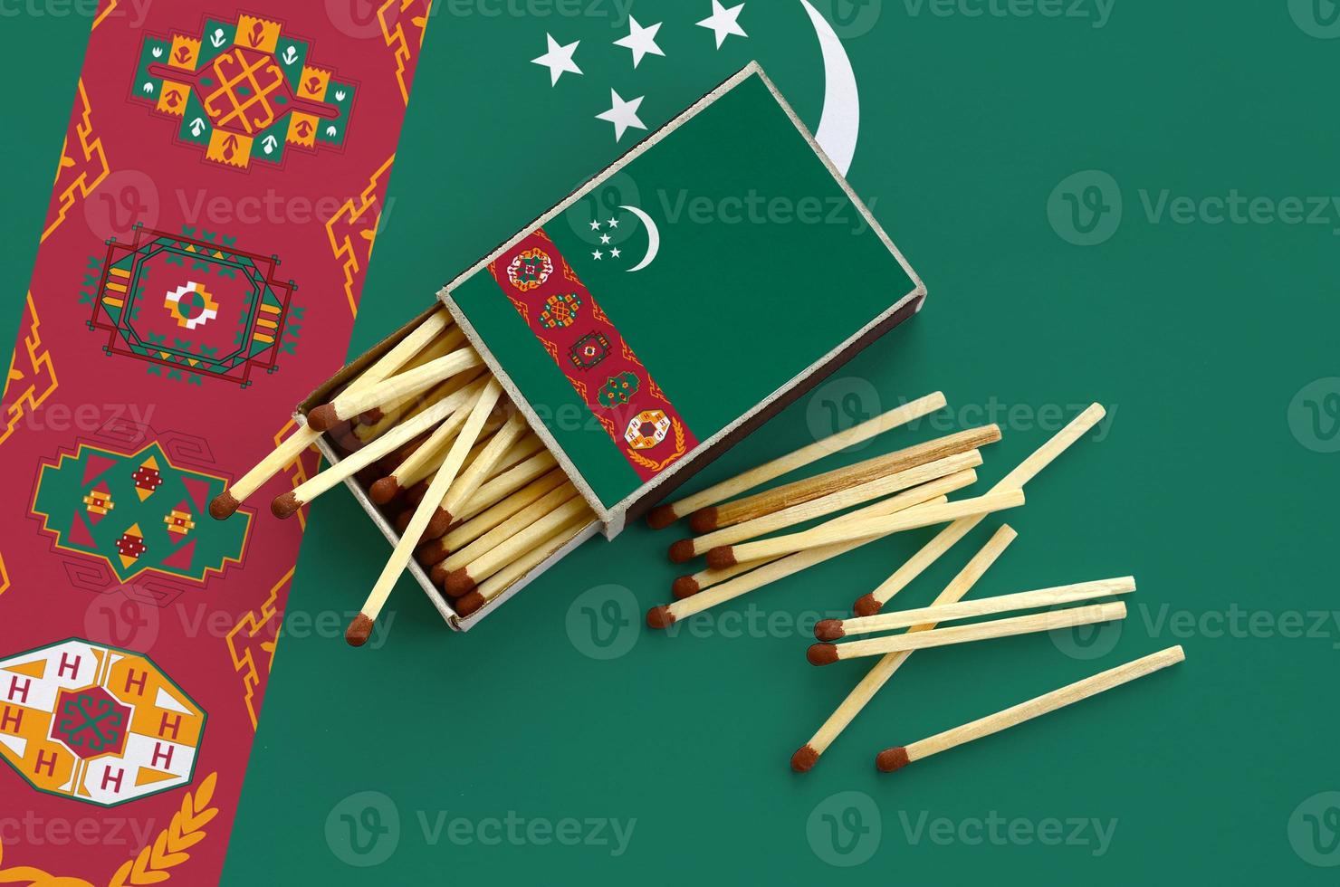 Turkmenistan flag  is shown on an open matchbox, from which several matches fall and lies on a large flag photo