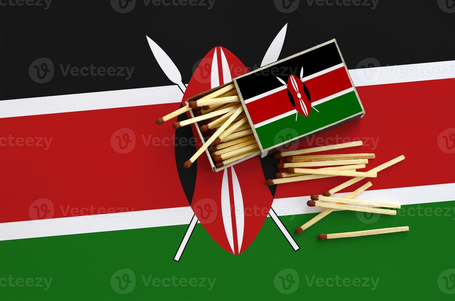Kenya flag  is shown on an open matchbox, from which several matches fall and lies on a large flag photo