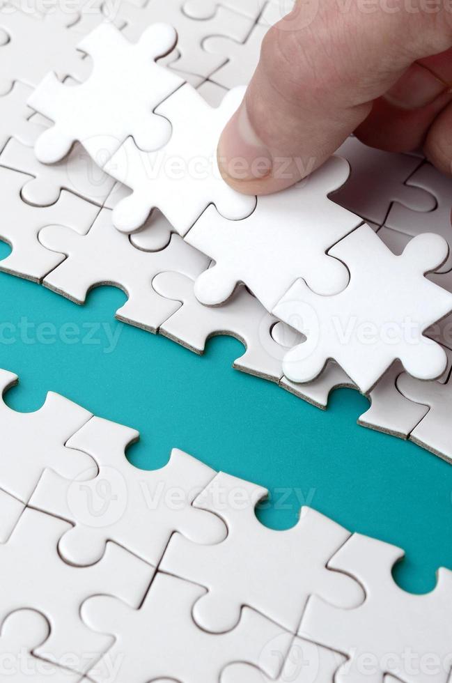 The human hand paves the way to the surface of the jigsaw puzzle, forming a blue space. The concept of overcoming the difficulties on the way to success photo