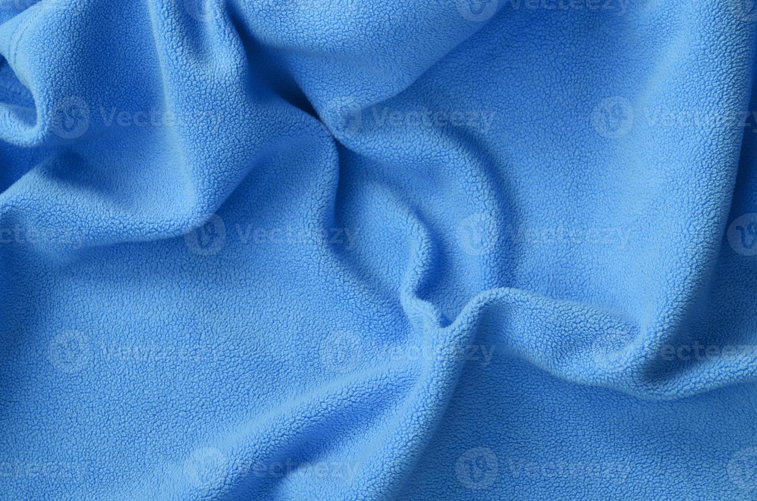 The blanket of furry blue fleece fabric. A background of light blue soft plush fleece material with a lot of relief folds photo