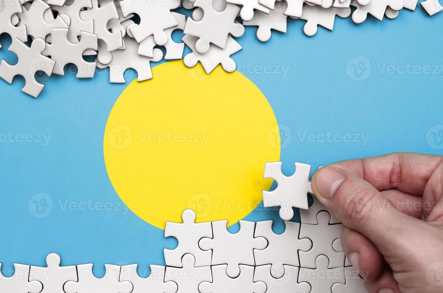 Palau flag  is depicted on a table on which the human hand folds a puzzle of white color photo