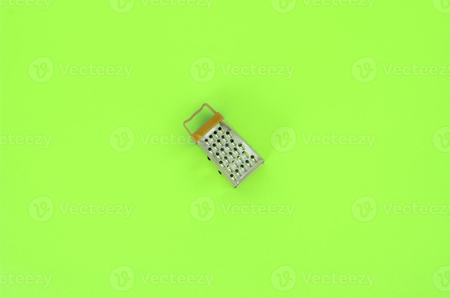 Stainless steel grater lies on a pastel colored paper. Kitchen accessories. Tools for cooking. Flat lay top view photo