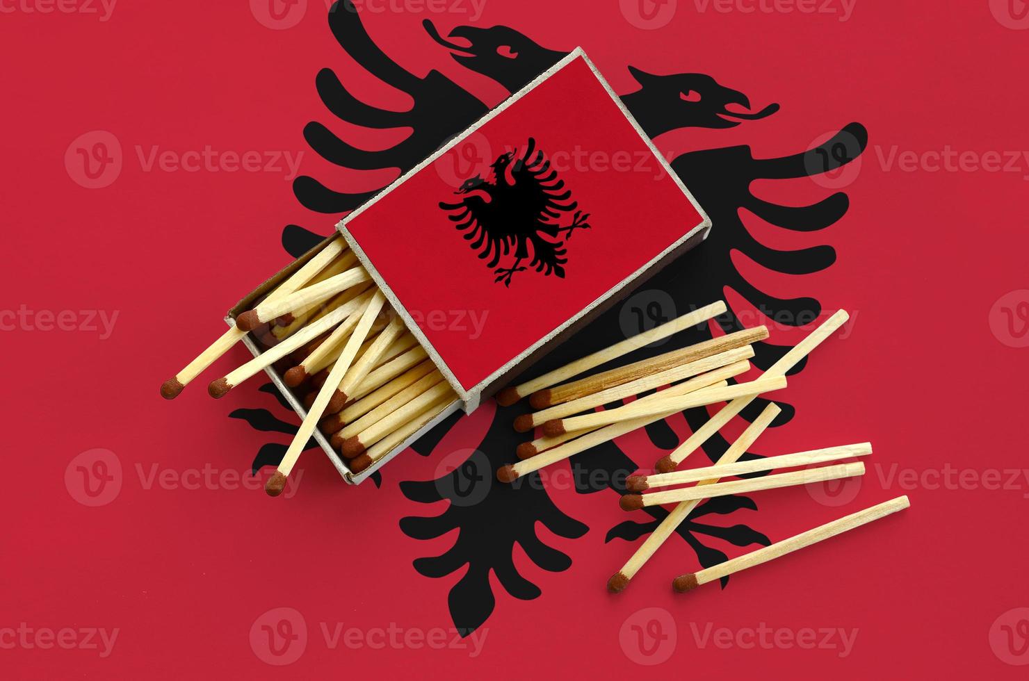 Albania flag  is shown on an open matchbox, from which several matches fall and lies on a large flag photo