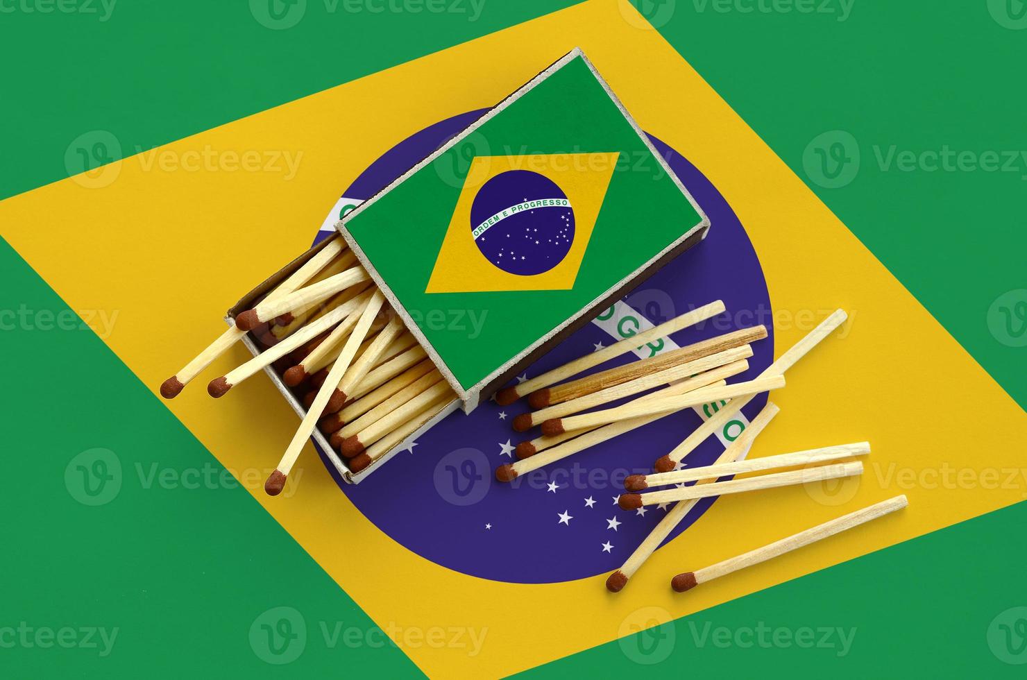 Brazil flag  is shown on an open matchbox, from which several matches fall and lies on a large flag photo